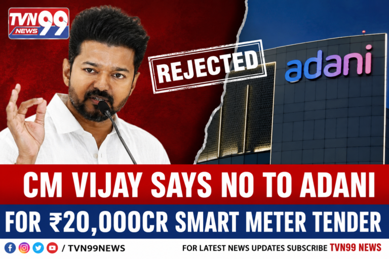 Tamil Nadu Chief Minister M.K. Vijay speaking during a public address alongside an Adani Group building, highlighting the controversy surrounding the reported rejection of the ₹20,000 crore smart meter tender project.
